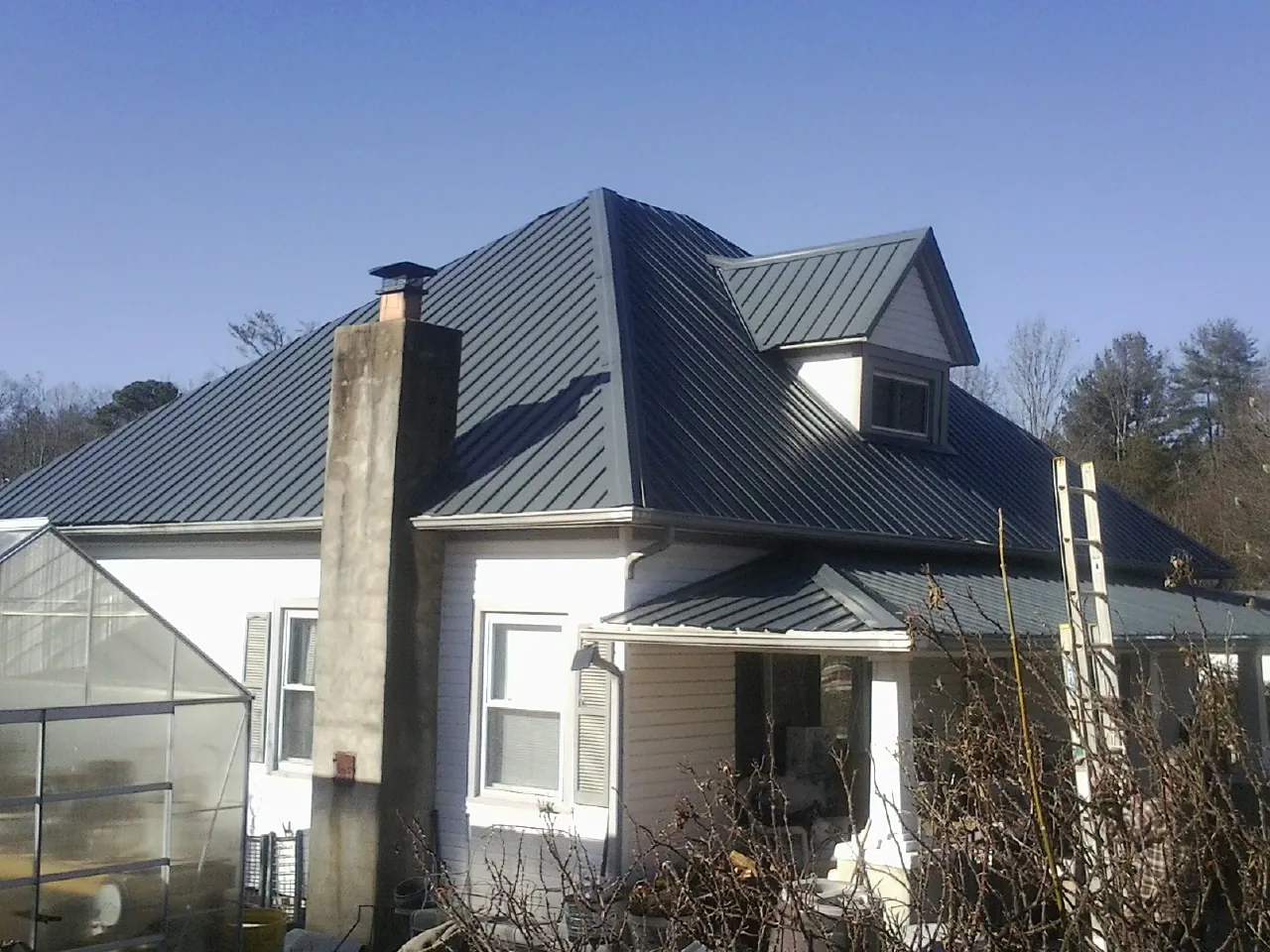 Dark blue standing seam metal roof on a white farmhouse with dormer — Slate & Tile Roof Repair by Roofing Brothers in Grand Rapids